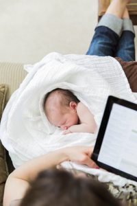 Mother reads digital tablet with sleeping baby in lap